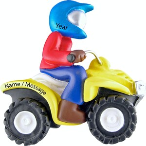 May include: A yellow ATV with a blue helmet wearing rider. The ATV has a white name/message area and the helmet has the word "Year" on it.