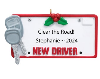 May include: Red and white Christmas ornament shaped like a license plate with the text "Clear the Road! Stephanie ~ 2024 NEW DRIVER" and a pair of silver keys on the left side.