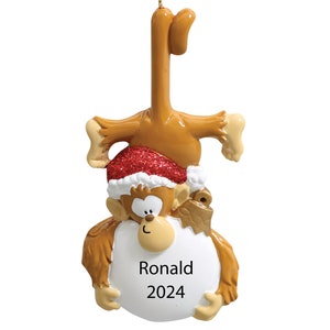 May include: A brown monkey Christmas ornament with a red Santa hat and a white circle with the name "Ronald" and the year "2024" written on it.