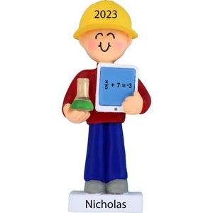 May include: A personalized Christmas ornament featuring a cartoon figure wearing a yellow hard hat and red shirt, holding a tablet with the equation 'x/5 + 7 = 3' and a beaker. The ornament has the name 'Nicholas' and the year '2023' on it.