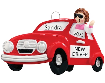 May include: A red car ornament with a person wearing sunglasses waving from the driver's seat. The car has the name "Sandra" and the year "2023" on it, with "NEW DRIVER" displayed on the side.