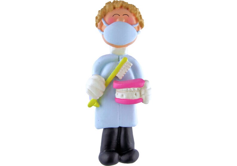 May include: A blue and white figurine of a dentist wearing a blue face mask and holding a toothbrush and a pink set of dentures.