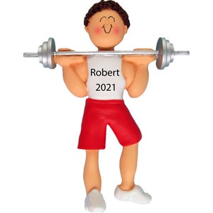May include: A personalized Christmas ornament featuring a cartoon man lifting a barbell. He is wearing a white tank top with the name "Robert" and the year "2021" printed on it. He is also wearing red shorts and white sneakers.