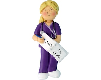 May include: Purple scrubs ornament with a blonde female figure holding a notepad with the year 2023 and the text "RN Linda".