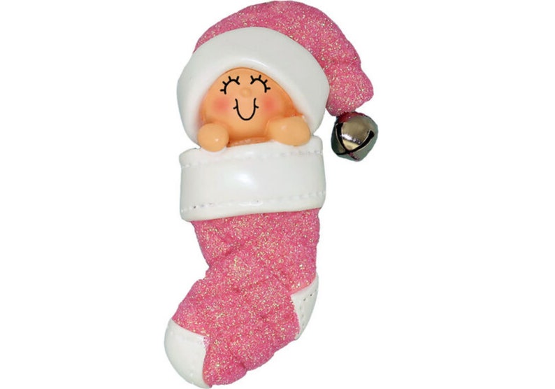 May include: Pink glitter stocking ornament with a baby doll inside wearing a white hat and a bell.