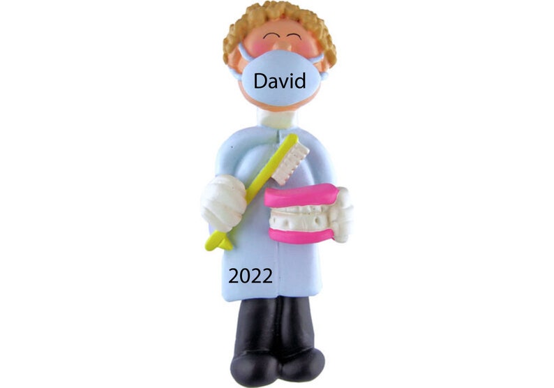 May include: A blue and white personalized ornament of a dentist holding a toothbrush and a set of dentures. The ornament has the name "David" on the face mask and the year "2022" on the bottom.