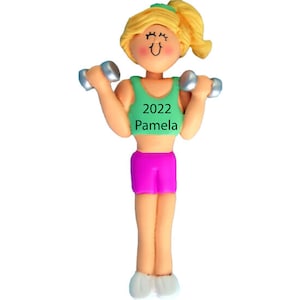 May include: A green and pink personalized ornament of a woman lifting weights. The ornament has the text "2022 Pamela" on the front.