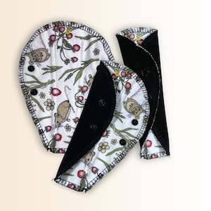 May include: Three reusable cloth pads with a white background and a pattern of mice, strawberries, and flowers. The pads have black fabric on the back side.