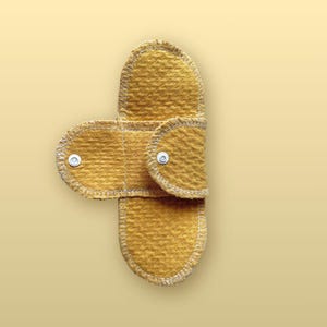 Open Golden Sand reusable cloth pad with wings spread outward, showing two white snap closures, rounded ends, organic cotton fabric, and white stitched edges.