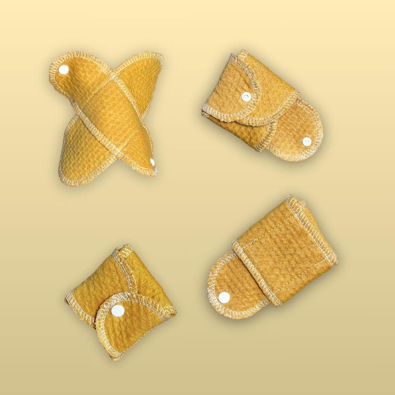 Four views of Golden Sand reusable cloth pads folded and snapped for compact storage, showing the wings, white snaps, stitching, and soft organic cotton fabric.