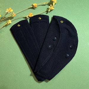 May include: Three black fabric pads with a gold embroidered letter G on each pad. The pad on the right has three black snaps.