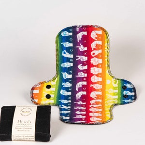 May include: A reusable cloth menstrual pad with a rainbow background and white sign language alphabet printed on it. The pad is shown with a black reusable charcoal pad.
