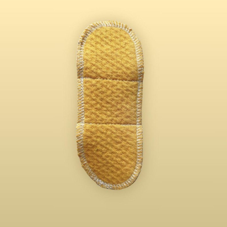 Full view of the Golden Sand organic cotton absorbent side of a 7.5-inch reusable cloth pad, showing its rounded shape, soft textured surface, sections, and white edge stitching.
