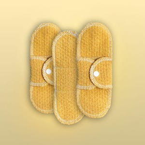 Three Golden Sand reusable cloth pads made with organic cotton, arranged together to show the long rounded shape, wings, white stitching, and snap closures.