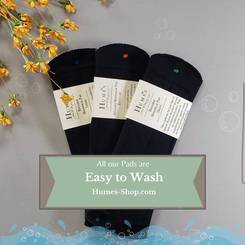 May include: Three black reusable menstrual pads with white labels, each with a different colored dot. The pads are labeled "Liners", "Regular", and "Heavy". Text on the image reads "All our Pads are Easy to Wash" and "Humes-Shop.com".