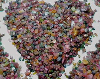 May include: A heart shape made of small, colorful gemstones. The gemstones are a mix of red, pink, green, and black.