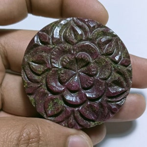 Puede incluir: Un colgante de rubí tallado con un diseño floral. El colgante es de color rojo intenso con acentos verdes.