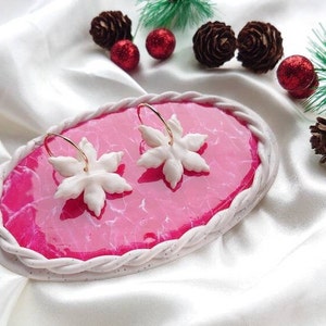 May include: A pair of white snowflake earrings with gold hoops on a pink and white display stand.