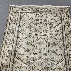 May include: A vintage rug with a light beige background and a brown and blue geometric pattern. The rug has a fringe border.