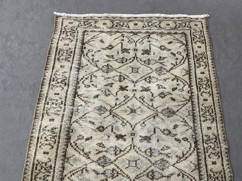 May include: A vintage rug with a light beige background and a brown and blue geometric pattern. The rug has a fringe border.