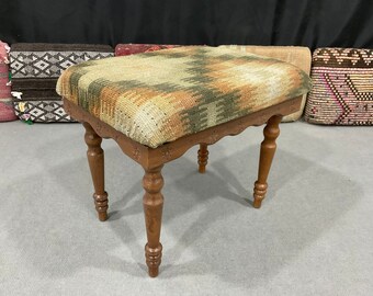 May include: A wooden stool with a woven tapestry seat cushion. The cushion has a geometric pattern in shades of brown, green, and orange.