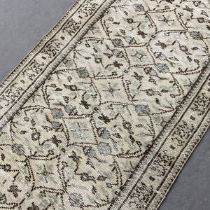 May include: A white and brown patterned runner rug with a geometric design. The rug has a fringe border.