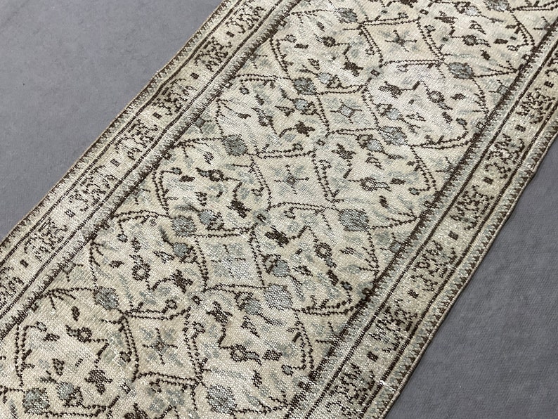 May include: A white and brown patterned runner rug with a geometric design. The rug has a fringe border.