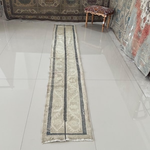 May include: A long, narrow, off-white rug with a dark gray geometric pattern. The rug has a faded, vintage look.