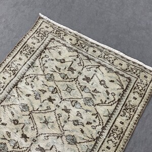 May include: A vintage rug with a beige background and a brown geometric pattern. The rug has a fringed edge.
