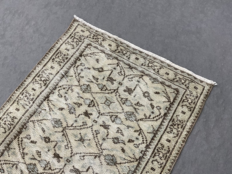 May include: A vintage rug with a beige background and a brown geometric pattern. The rug has a fringed edge.