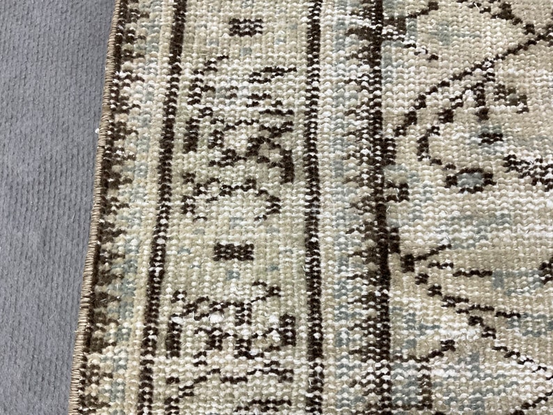 May include: Close-up of a beige and brown patterned rug with a fringe border. The rug has a traditional design with intricate details.