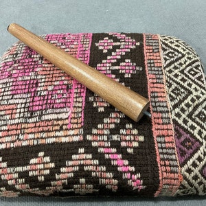 May include: A rectangular, upholstered ottoman with a brown, pink, and white patterned design. A wooden furniture leg is placed on top. The ottoman's fabric features geometric and floral motifs, creating a textured appearance.