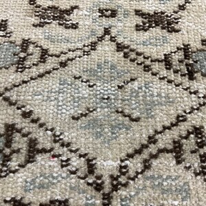 May include: Close-up of a beige rug with a geometric pattern in brown and light blue. The pattern is made up of repeating diamonds and squares.