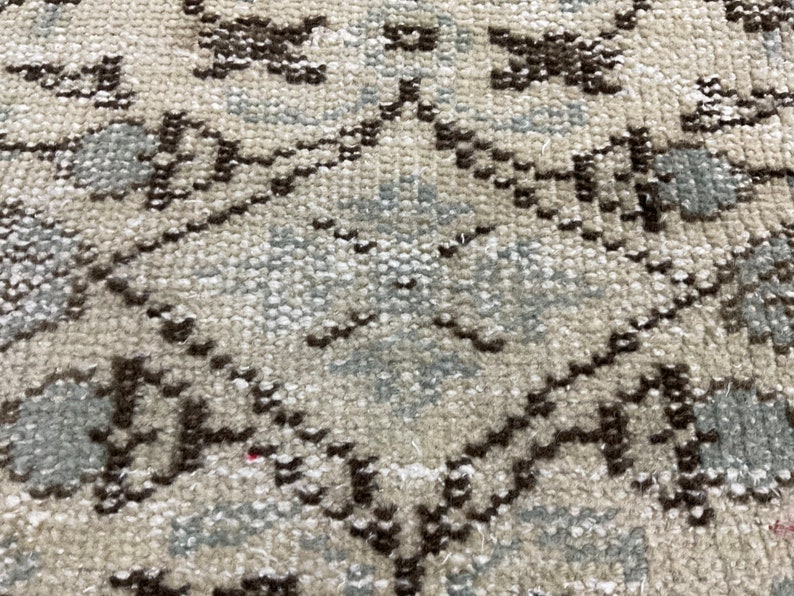May include: Close-up of a beige rug with a geometric pattern in brown and light blue. The pattern is made up of repeating diamonds and squares.