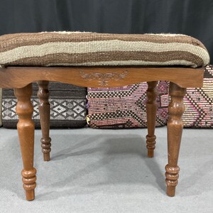 May include: A wooden stool with a brown and white striped cushion. The stool has four turned legs and a carved design on the top.