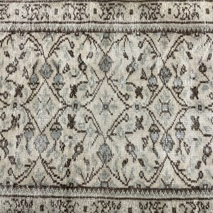 May include: A vintage rug with a geometric pattern in shades of brown and white. The rug has a distressed look and is made of wool.