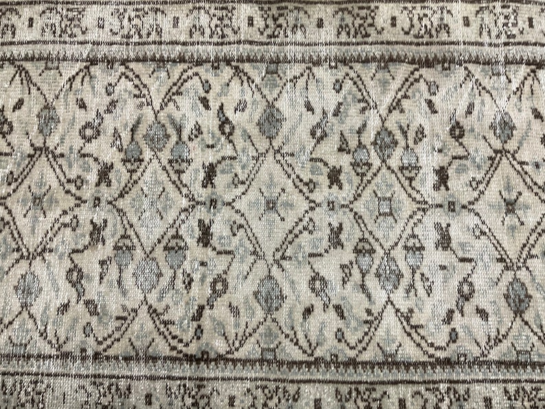 May include: A vintage rug with a geometric pattern in shades of brown and white. The rug has a distressed look and is made of wool.