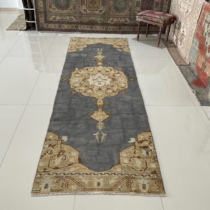 May include: A rectangular, vintage-style rug with a central medallion design. The rug features a dark gray field with beige and cream-colored accents. The intricate pattern includes floral and geometric elements, creating a classic, elegant look. The rug is displayed on a tiled floor.