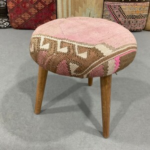 May include: A pink and brown patterned stool with three wooden legs.