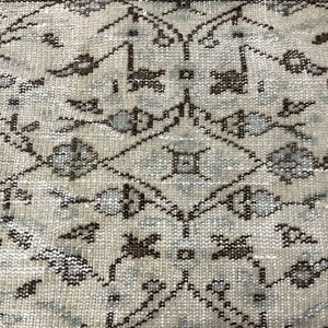 May include: A close-up of a beige rug with a repeating pattern of brown and light blue floral designs.