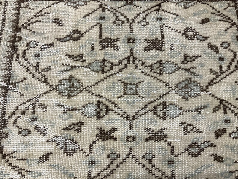 May include: A close-up of a beige rug with a repeating pattern of brown and light blue floral designs.