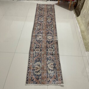 Könnte beinhalten: Ein langer, schmaler Teppich mit traditionellem persischem Design. Der Teppich hat einen dunkelblauen Hintergrund mit komplizierten Mustern in Rosa-, Beige- und Cremetönen.