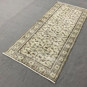 May include: A beige and brown patterned rug with a geometric design. The rug has a fringed edge and is made of a soft, woven material.