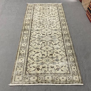 May include: A vintage cream-colored rug with a brown floral pattern. The rug has a fringed edge and is approximately 2.5 feet wide and 8 feet long.