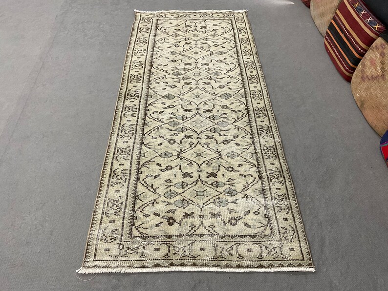 May include: A vintage cream-colored rug with a brown floral pattern. The rug has a fringed edge and is approximately 2.5 feet wide and 8 feet long.