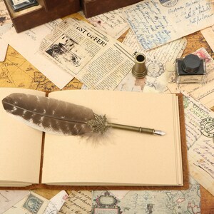 Puede incluir: Un diario de estilo vintage con una cubierta de cuero marr&oacute;n y p&aacute;ginas en blanco. Una pluma con una pluma y una punta de metal descansa sobre las p&aacute;ginas abiertas. El diario est&aacute; rodeado de mapas antiguos, cartas y sellos.