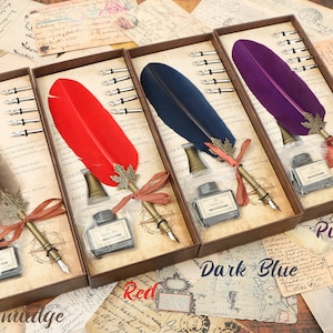 Puede incluir: Tres juegos de plumas de caligraf&iacute;a en cajas de madera. Cada juego incluye una pluma de pluma, tintero y cinco plumillas. Las plumas son rojas, azul oscuro y moradas. Las cajas tienen las palabras "Smudge", "Red", "Dark Blue" y "Purple" impresas en ellas.