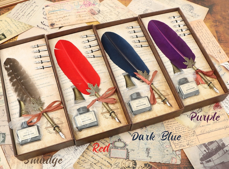 Puede incluir: Tres juegos de plumas de caligraf&iacute;a en cajas de madera. Cada juego incluye una pluma de pluma, tintero y cinco plumillas. Las plumas son rojas, azul oscuro y moradas. Las cajas tienen las palabras "Smudge", "Red", "Dark Blue" y "Purple" impresas en ellas.