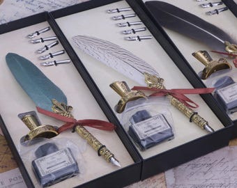 Peut inclure: Trois boîtes-cadeaux noires avec des garnitures dorées, chacune contenant un ensemble de calligraphie avec un stylo plume, un encrier et des pointes. Les plumes sont blanches, vertes et grises.