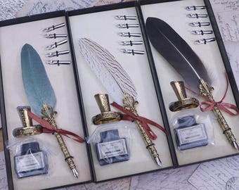 Peut inclure: Trois ensembles de kits de calligraphie dans des boîtes noires. Chaque ensemble comprend un stylo plume, un flacon d'encre et des pointes. Les stylos sont décorés d'accents dorés. Les plumes sont blanches, bleues et noires.